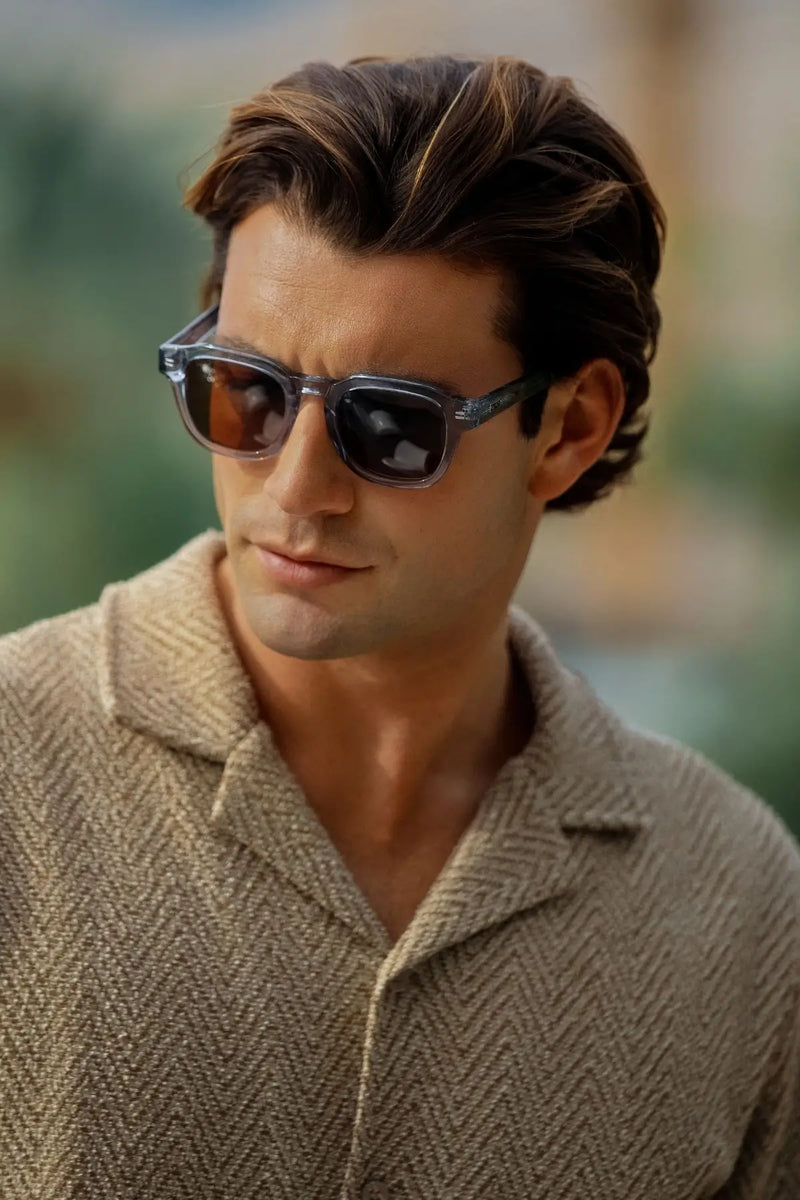 Model wearing WMP Eyewear Nelson sunglasses in Denim Blue, featuring a translucent blue frame with brown lenses.
